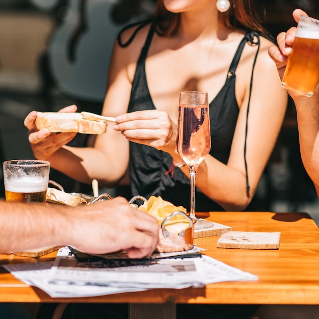 Grupo de amigos sentados en una terraza de verano con cerveza y champán en sus manos y bocadillos en la mesa