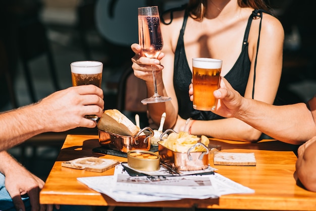 Foto grupo de amigos sentados en una terraza de verano con cerveza y vino en sus manos y bocadillos en la mesa