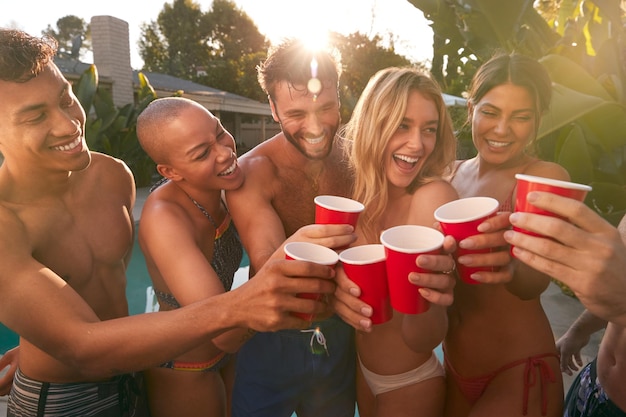 Grupo de amigos sonrientes al aire libre haciendo un brindis con cerveza y disfrutando de la fiesta en la piscina de verano