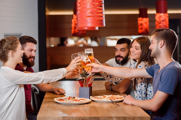 Grupo de amigos tintineando vasos de cerveza en pizzería