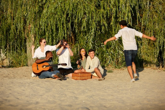 Grupo de amigos tintineo de vasos de cerveza durante un picnic en la playa