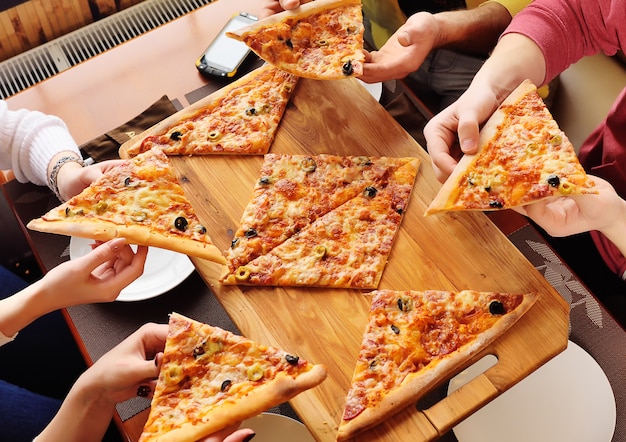 Un grupo de amigos toma una pizza fresca y caliente sentada en un café. Manos con rebanadas de primer plano de pizza.