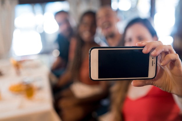 Grupo de amigos tomando un selfie con un teléfono móvil en un restaurante.