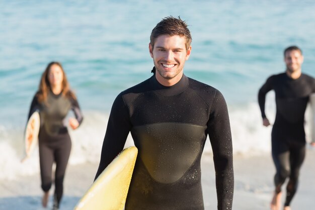 Grupo de amigos en trajes de neopreno con una tabla de surf en un día soleado