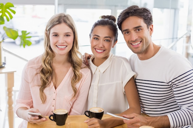 Grupo de amigos usando el teléfono móvil mientras toma una taza de café