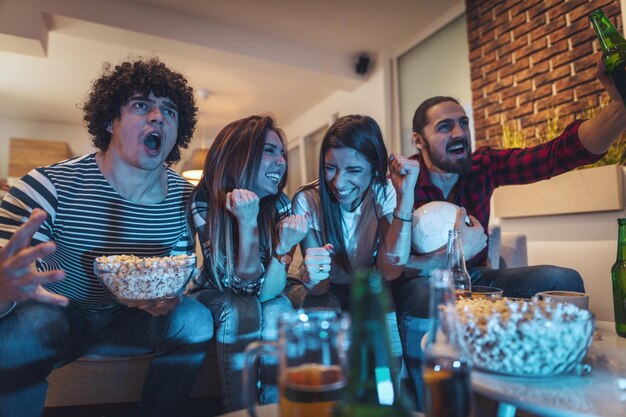 Un grupo de amigos ve la retransmisión de un evento deportivo. Se sientan frente al televisor en la sala de estar, comen bocadillos, beben cerveza y animan al equipo favorito.