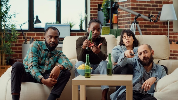 Grupo de amigos viendo películas de acción en el programa del canal de televisión, bebiendo cerveza de botellas. Personas que disfrutan de actividades de ocio con bebidas y películas o espectáculos de televisión. Disparo de trípode.