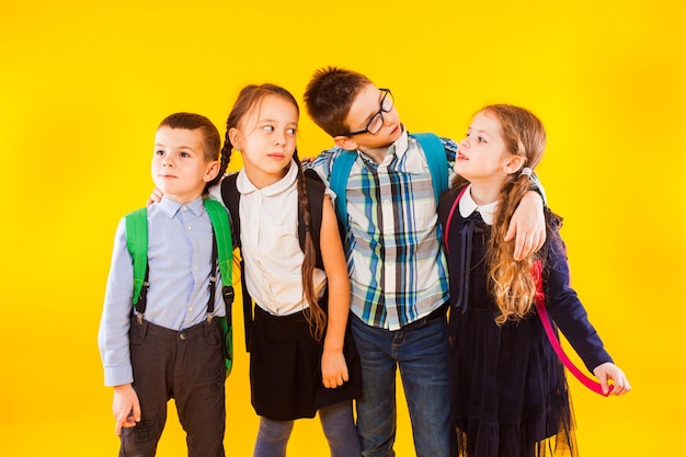 El grupo amistoso de escolares está de pie con mochilas en un fondo amarillo