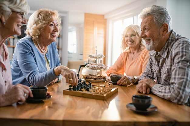 Grupo de ancianos felices comunicándose mientras juegan al ajedrez en casa El foco está en la mujer con suéter azul