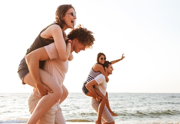 Grupo animado de amigos amando casais caminhando ao ar livre na praia se divertindo