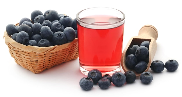 Grupo de arándanos frescos con jugo en un vaso sobre fondo blanco.