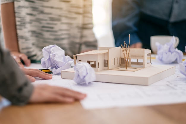 El grupo de un arquitecto se siente estresado después de trabajar en el modelo de arquitectura junto con el papel de dibujo de la tienda en la mesa de la oficina