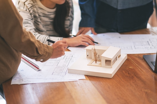 Grupo de un arquitecto trabajando y discutiendo sobre un modelo de arquitectura junto con el papel de dibujo de la tienda sobre la mesa en la oficina