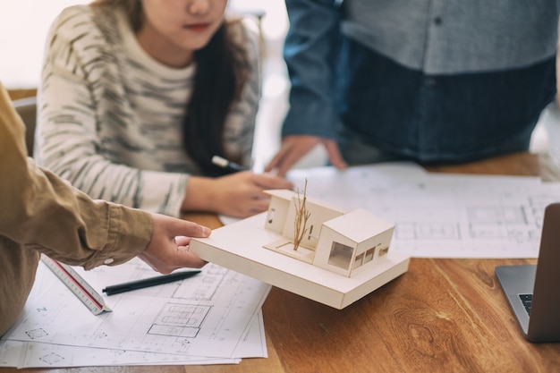 Grupo de un arquitecto trabajando y discutiendo sobre un modelo de arquitectura junto con el papel de dibujo de la tienda sobre la mesa en la oficina