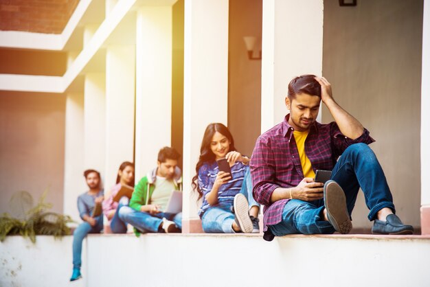 Grupo asiático indio de estudiantes universitarios que utilizan teléfonos inteligentes para las redes sociales, mensajes de texto, viendo videos