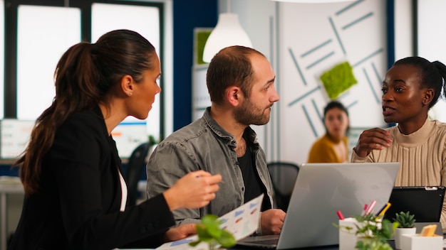 Grupo autêntico e diverso de empresários entusiasmados, profissionais de marketing, usando um laptop, discutindo durante a reunião de idéias de projetos, discutindo sobre a estratégia de uma empresa de startups sentados na offi