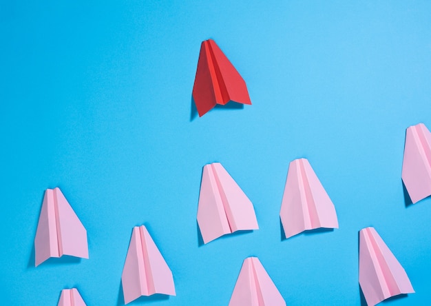 Un grupo de aviones de papel rosa sigue al primer rojo contra una superficie azul. El concepto de unir un equipo para lograr metas, un líder fuerte, un grupo altamente efectivo.