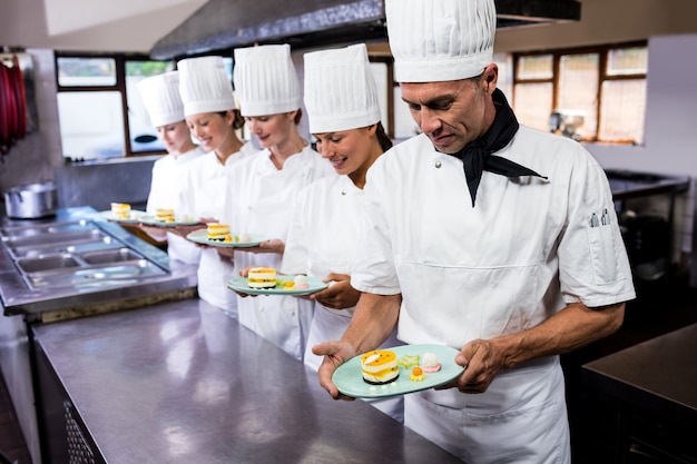 Grupo de chefs con plato de deliciosos postres en la cocina