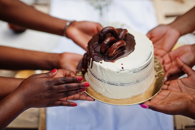 Grupo de chicas afroamericanas celebrando la fiesta de cumpleaños al aire libre. Manos negras con pastel.