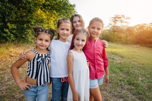 Foto un grupo de chicas alegres están sonriendo y jugando en el parque durante la puesta de sol. campamento de verano para niños.