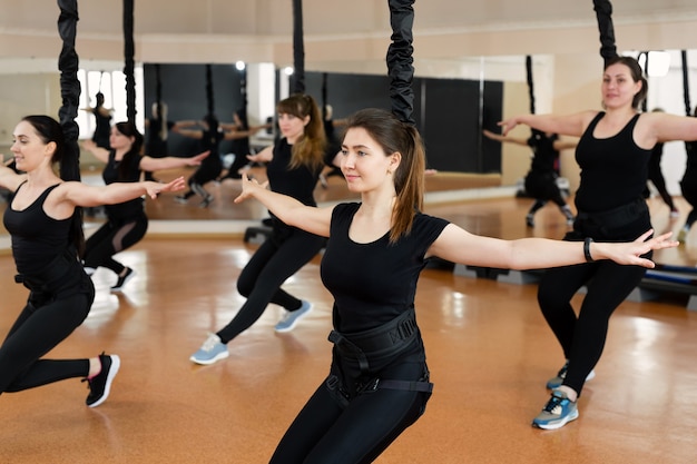 Grupo de chicas de deportes activos en ropa deportiva negra se dedican a la aptitud del periquito en el gimnasio