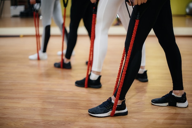 Un grupo de chicas jóvenes se dedica a la actividad física con un expansor bajo la guía de un entrenador experimentado. Fitness, estilo de vida saludable.