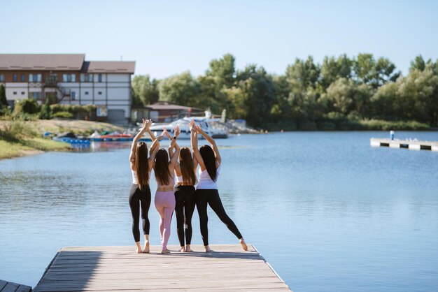 Grupo de chicas jóvenes haciendo yoga al aire libre y cerca del agua