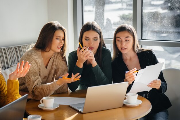 Un grupo de chicas jóvenes se sienta en una oficina frente a las computadoras y discute proyectos. Comunicación y formación online.