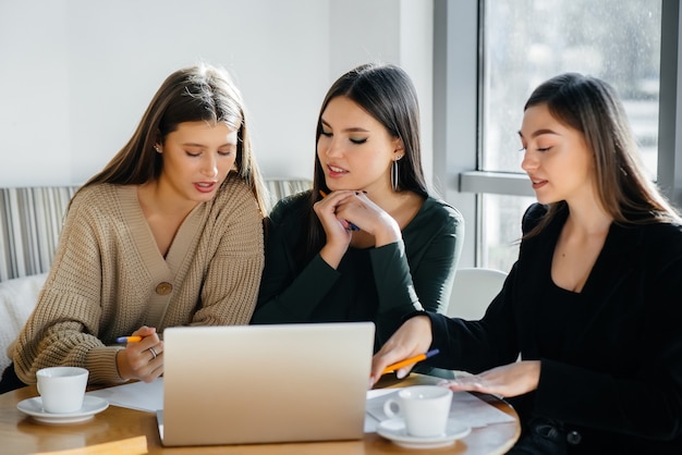 Un grupo de chicas jóvenes se sienta en una oficina frente a las computadoras y discute proyectos. Comunicación y formación online.