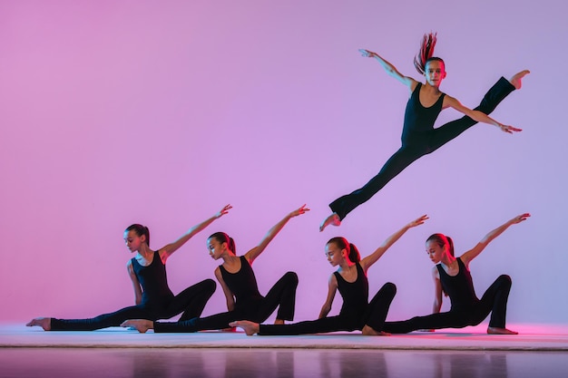 Grupo de cinco adolescentes balrins en trajes ajustados negros están bailando konteporari moderno sobre un fondo lila