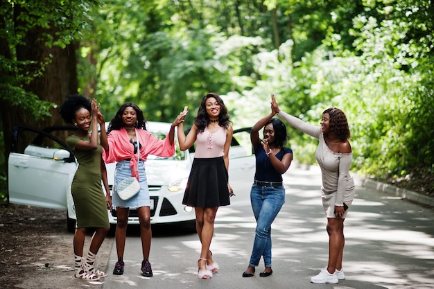 Grupo de cinco afroamericanos felices caminando contra un auto blanco