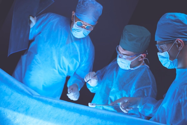 Grupo de cirujanos en el trabajo en quirófano tonificado en azul Equipo médico realizando operación