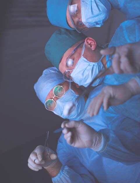 Foto grupo de cirujanos en el trabajo en quirófano tonificado en azul equipo médico realizando operación