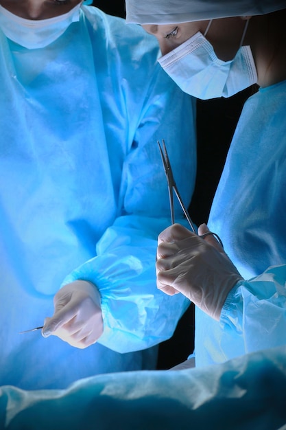 Grupo de cirujanos en el trabajo en quirófano en tonos de azul. Equipo médico realizando operación