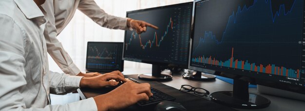 Grupo de comerciantes discutiendo en el escritorio de la oficina monitoreando el mercado de valores en el monitor en el lugar de trabajo de la oficina Empresario y corredor analizando el gráfico de acciones juntos en la empresa de comercio de acciones Pionero