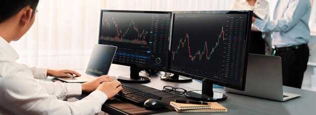 Grupo de comerciantes discutiendo en el escritorio de la oficina monitoreando el mercado de valores en el monitor en el lugar de trabajo de la oficina Empresario y corredor analizando el gráfico de acciones juntos en la empresa de comercio de acciones Pionero