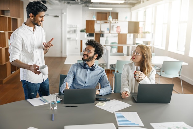 Grupo de compañeros de trabajo sonrientes que trabajan juntos analizando los gráficos en la oficina moderna