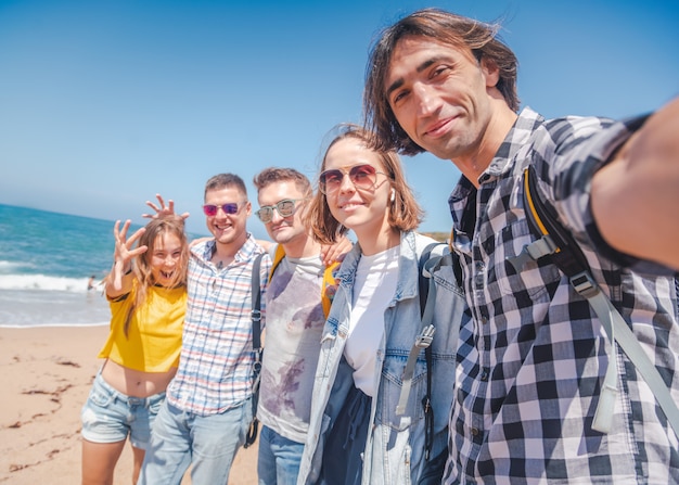 Grupo de la compañía de jóvenes abrazos felices felices, estudiantes hombres y mujeres en una playa soleada, concepto de día de amistad de viaje de vacaciones