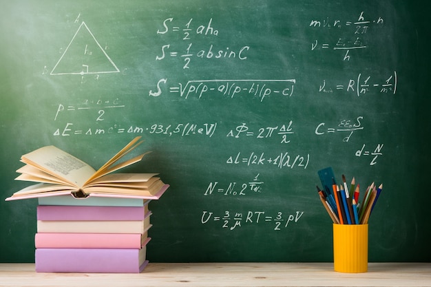 Grupo de concepto de educación y lectura de libros coloridos sobre la mesa de madera en el fondo de la pizarra del aula