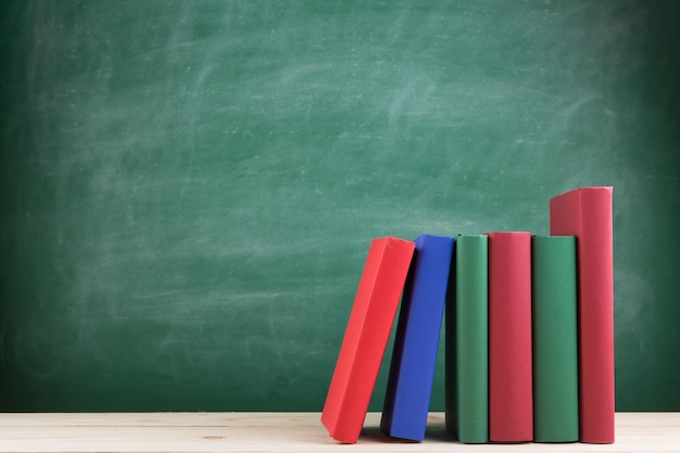 Grupo de concepto de educación y lectura de libros coloridos sobre la mesa de madera en el fondo de la pizarra del aula