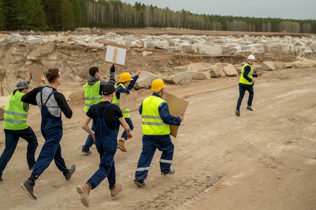 Grupo de constructores descontentos con carteles que se ejecutan después del contratista a lo largo del sitio de construcción