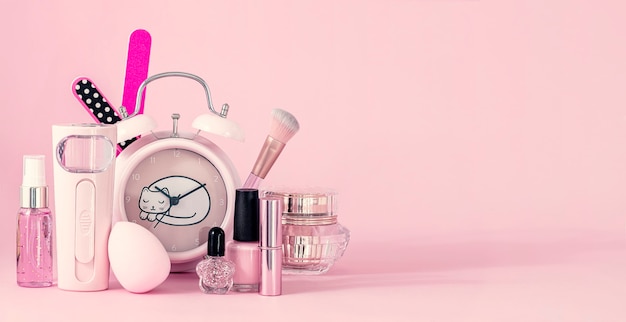 Grupo de cosméticos de maquillaje profesional y reloj antiguo sobre fondo rosa con espacio de copia