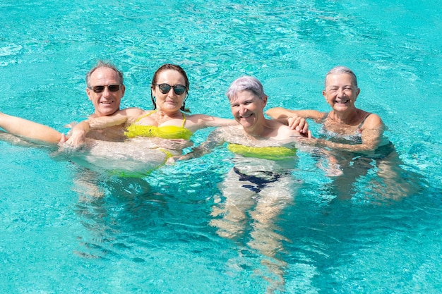 Grupo de cuatro amigos alegres divirtiéndose en la piscina al aire libre bajo el sol Vacaciones y relajación