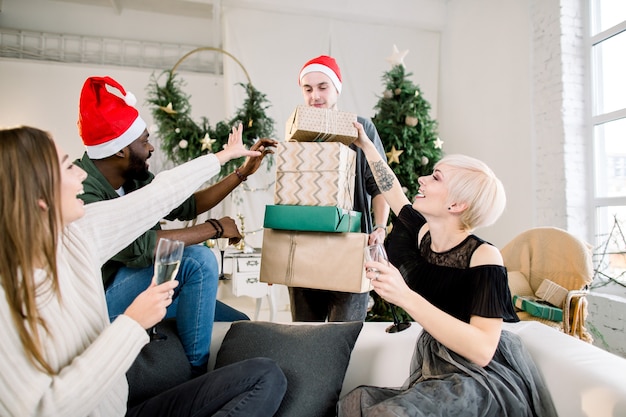 Grupo de cuatro amigos jóvenes felices riendo y compartiendo regalos de Navidad