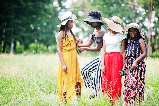 Grupo de cuatro hermosas mujeres afroamericanas usan sombrero de verano pasando tiempo en la hierba verde en el parque