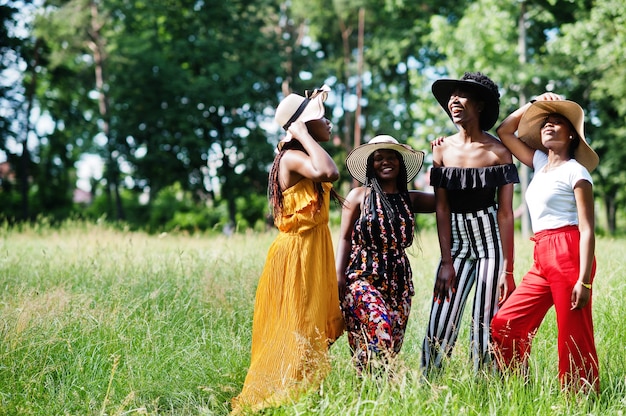 Grupo de cuatro hermosas mujeres usan sombreros de verano pasando tiempo en la hierba verde en el parque