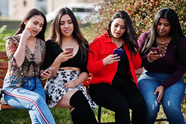 Un grupo de cuatro muchachas latinas felices y bonitas de Ecuador posó en la calle mirando teléfonos móviles.