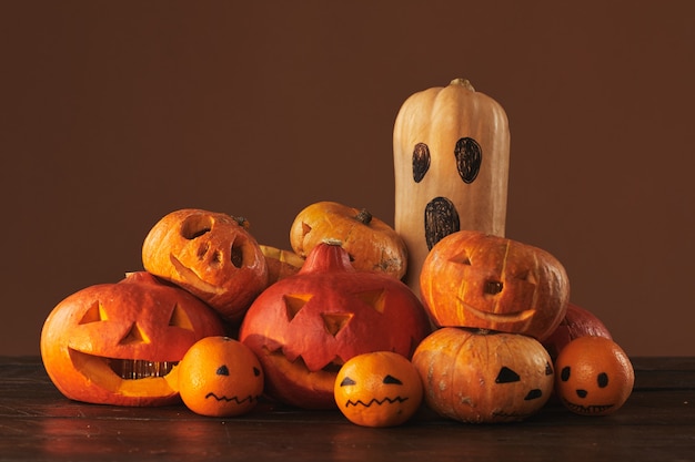 Grupo de abóboras, cabaças e tangerinas esculpidas e pintadas para decoração de festa de Halloween em superfície marrom