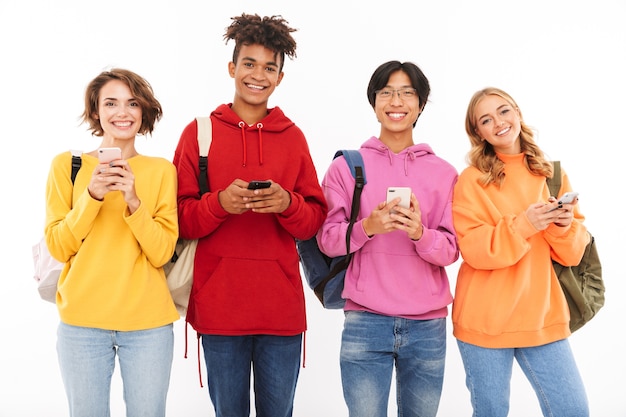 Foto grupo de adolescentes alegres isolado, carregando mochilas, usando celulares