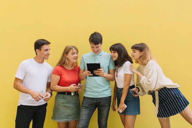 Grupo de adolescentes que usam seus telefones celulares e tabuleta em um fundo amarelo.